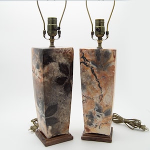 May include: Pair of decorative table lamps. Each lamp features a rectangular base with a unique pattern of brown, beige, and black tones. The lamps have a brass-colored neck and a brown wooden base. The lamps are designed for indoor use.