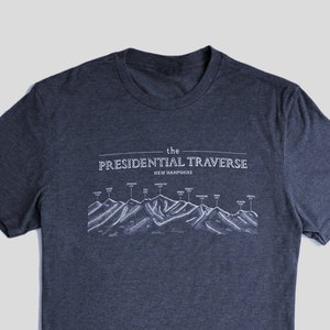 Op de afbeelding: Een donkerblauw t-shirt met een witte afbeelding van de Presidential Traverse in New Hampshire. De afbeelding toont een bergketen met de namen van de toppen die zijn gelabeld.