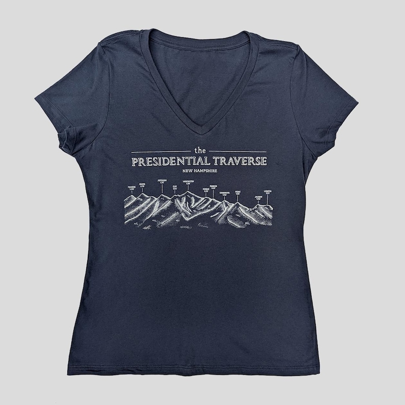 Op de afbeelding: Een marineblauw V-hals T-shirt met een witte afbeelding van de Presidential Traverse in New Hampshire. De afbeelding toont een bergketen met de namen van de toppen.
