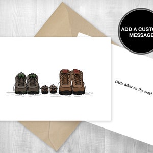 May include: A white card with a drawing of four pairs of hiking boots. The boots are brown, green, and tan. The card says "Little hiker on the way!" and "ADD A CUSTOM MESSAGE".