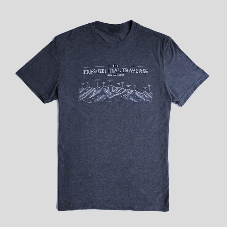 Op de afbeelding: Een donkerblauw t-shirt met een witte afbeelding van de Presidential Traverse in New Hampshire. De afbeelding toont een bergketen met de namen van de toppen die zijn gelabeld.