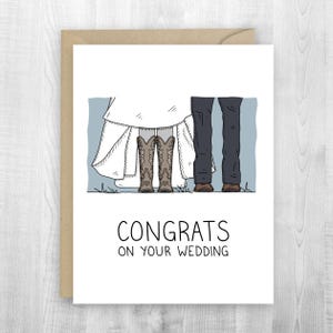 May include: A wedding greeting card with a white background and a brown envelope. The card features an illustration of a bride in a white dress and cowboy boots, and a groom in dark pants and brown shoes. The text reads "CONGRATS ON YOUR WEDDING."