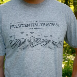 Op de afbeelding: Een grijs T-shirt met een zwarte afbeelding van de Presidential Traverse in New Hampshire. De afbeelding toont de bergketen met de namen van de toppen en hun hoogtes.