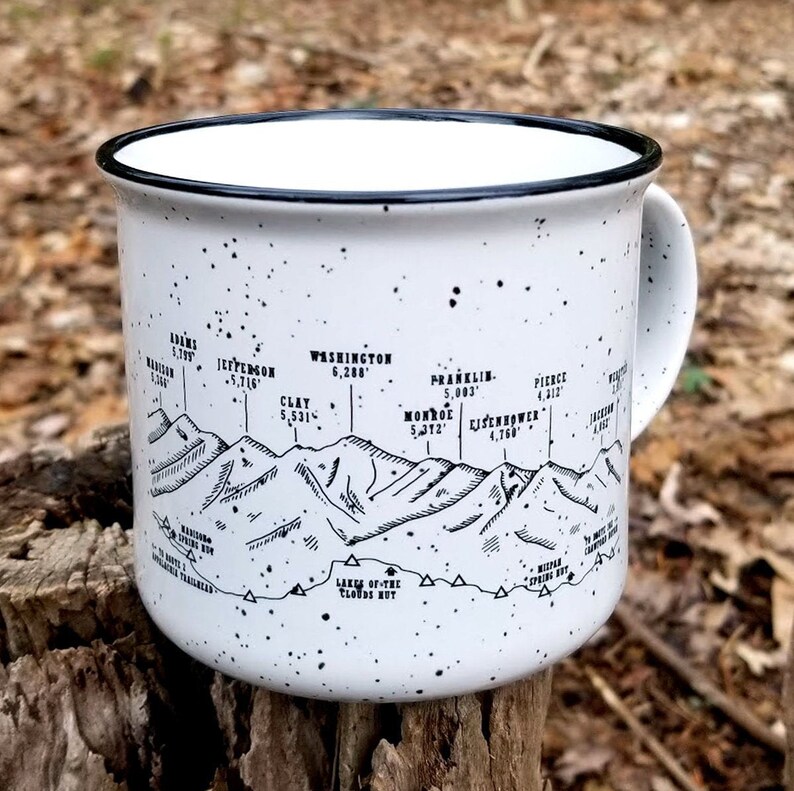 Puede incluir: Taza de camping de esmalte blanco con borde y asa negros. La taza presenta un gr&aacute;fico en blanco y negro de una cordillera con picos etiquetados con nombres y elevaciones. La taza tiene un patr&oacute;n moteado.