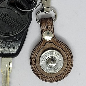 May include: A set of keys with a black key fob and a brown leather keychain. The keychain has a silver clasp and a circular design with the text "Wellington Co GA". The keys are on a white background.