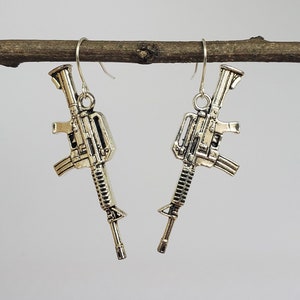 May include: A pair of silver earrings shaped like assault rifles hanging from a branch.