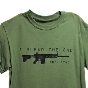 May include: A green t-shirt with a black silhouette of a rifle and the text "I PLEAD THE 2ND EST. 1789".