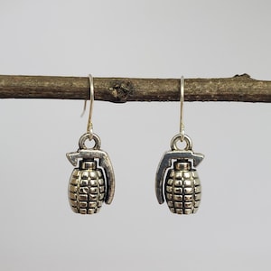 May include: A pair of silver dangle earrings shaped like hand grenades. The earrings are hanging from a branch.