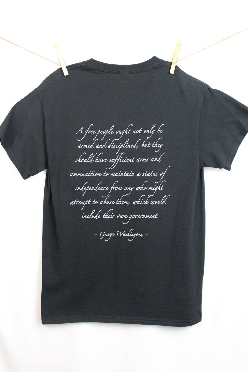 Puede incluir: Una camiseta gris oscura con una cita blanca de George Washington sobre la importancia de un pueblo libre armado y disciplinado. La cita dice: "Un pueblo libre no solo debe estar armado y disciplinado, sino que debe tener suficientes armas y municiones para mantener un estado de independencia de cualquiera que pueda intentar abusar de ellos, lo que incluir&iacute;a su propio gobierno. -George Washington- "