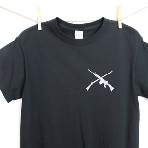 Puede incluir: Camiseta negra con un gr&aacute;fico blanco de dos rifles cruzados.