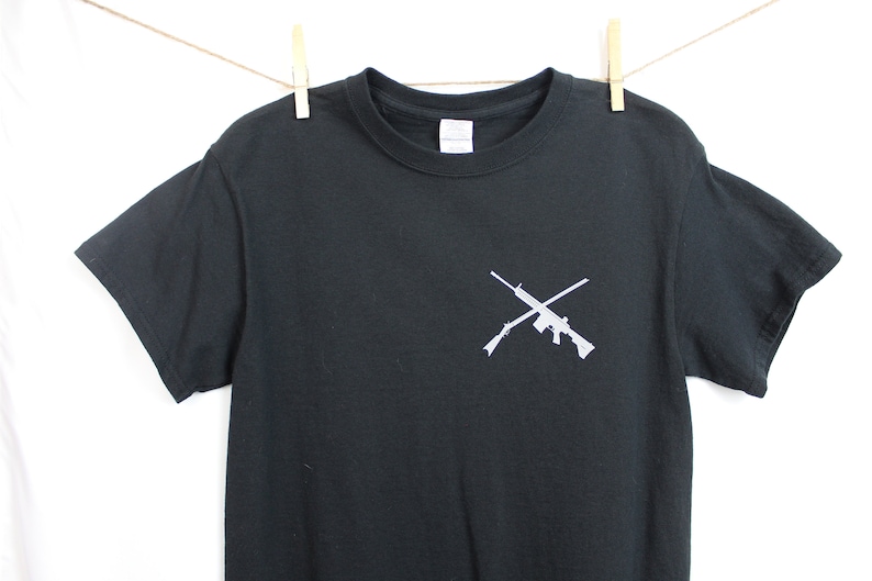 Puede incluir: Camiseta negra con un gr&aacute;fico blanco de dos rifles cruzados.