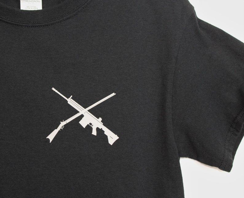 Puede incluir: Camiseta negra con una silueta blanca de dos rifles cruzados.