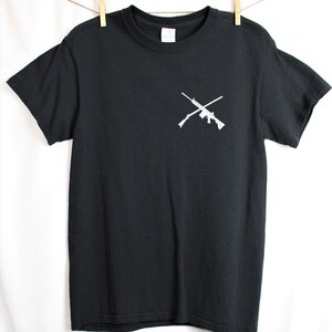 Puede incluir: Camiseta negra con un gr&aacute;fico blanco de dos rifles cruzados en el pecho.
