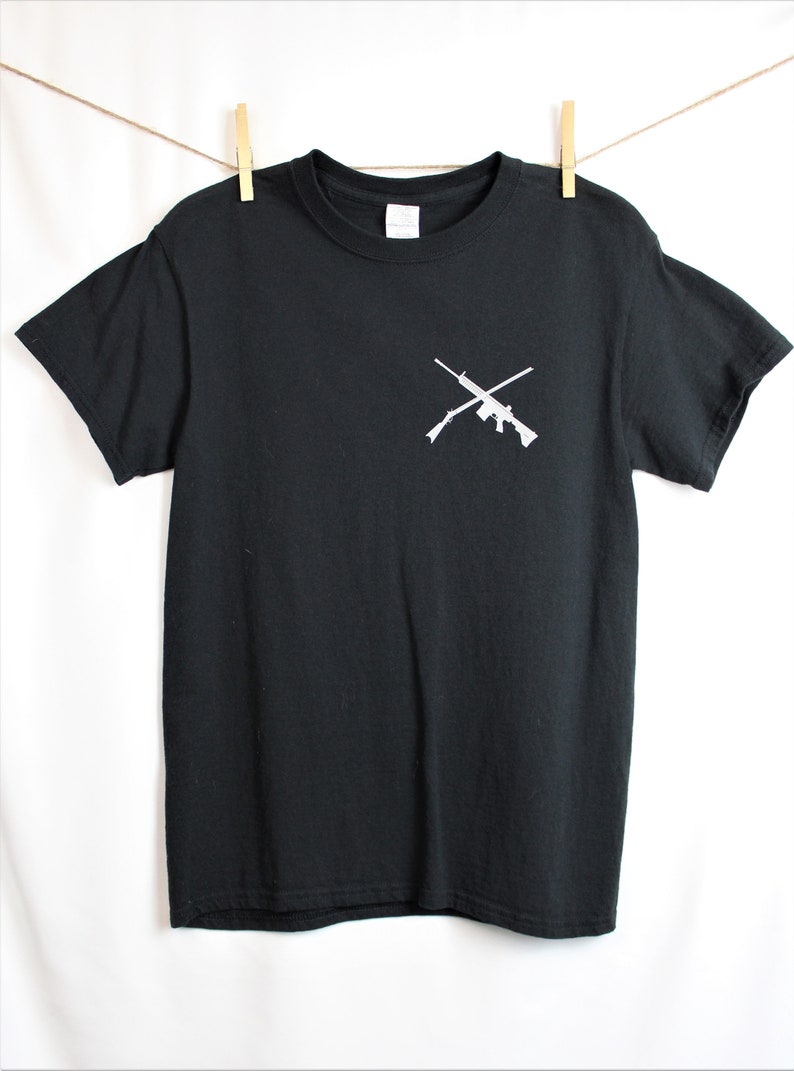 Puede incluir: Camiseta negra con un gr&aacute;fico blanco de dos rifles cruzados en el pecho.