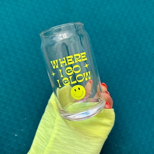 May include: A clear glass with a yellow smiley face and the text "WHERE I GO I GLOW" printed on it.
