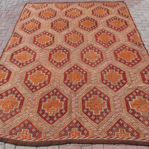 Könnte beinhalten: Ein antiker türkischer Teppich mit einem geometrischen Muster in Rot-, Orange- und Brauntönen. Der Teppich hat einen gewebten Rand und ist aus Wolle.