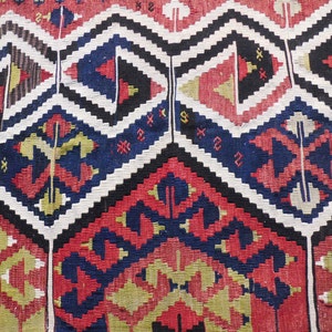May include: A close-up of a colorful woven rug with a geometric pattern in shades of red, blue, black, white, and yellow.