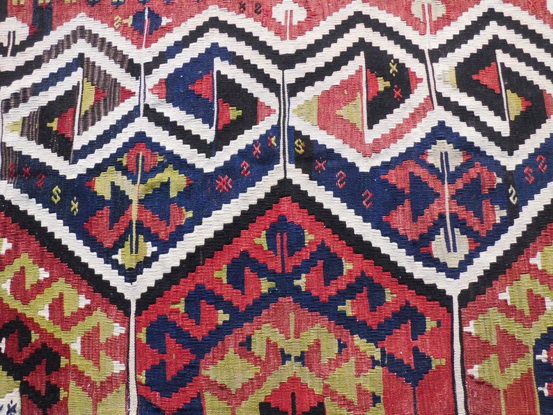 May include: A close-up of a colorful woven rug with a geometric pattern in shades of red, blue, black, white, and yellow.