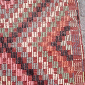 K&ouml;nnte beinhalten: Nahaufnahme eines roten, schwarzen, wei&szlig;en und gr&uuml;nen gemusterten Teppichs mit geometrischem Design. Der Teppich hat eine gewebte Textur.