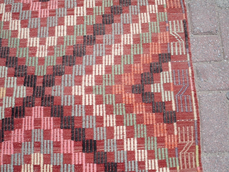 K&ouml;nnte beinhalten: Nahaufnahme eines roten, schwarzen, wei&szlig;en und gr&uuml;nen gemusterten Teppichs mit geometrischem Design. Der Teppich hat eine gewebte Textur.