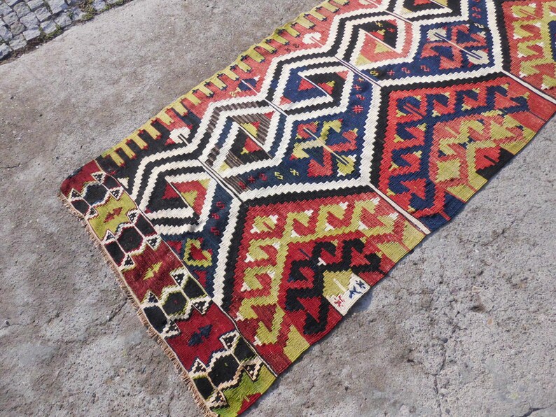 May include: A colorful, geometric patterned rug with a traditional design. The rug features a mix of red, yellow, blue, black, and white colors.
