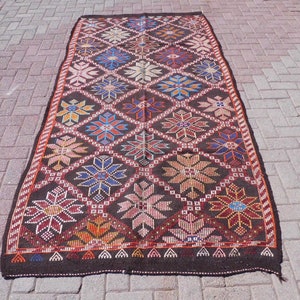 May include: A long, rectangular rug with a dark brown background and a repeating pattern of colorful flowers. The rug has a fringe border.