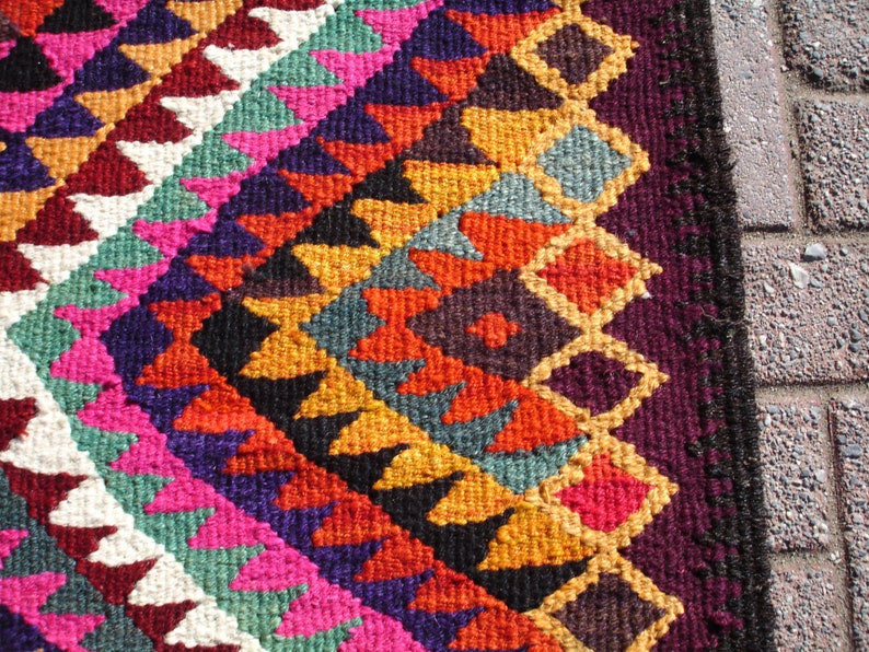 May include: A colorful rug with a geometric pattern in shades of red, orange, yellow, green, blue, purple, and white. The rug has a fringe border.