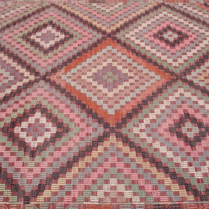 K&ouml;nnte beinhalten: Nahaufnahme eines bunten gewebten Teppichs mit einem geometrischen Muster aus Quadraten und Rauten in den Farben Rosa, Rot, Gr&uuml;n, Blau und Braun.