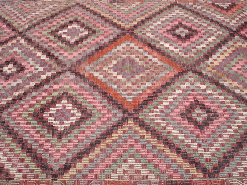 K&ouml;nnte beinhalten: Nahaufnahme eines bunten gewebten Teppichs mit einem geometrischen Muster aus Quadraten und Rauten in den Farben Rosa, Rot, Gr&uuml;n, Blau und Braun.