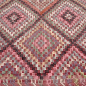 K&ouml;nnte beinhalten: Ein bunter Teppich mit einem geometrischen Muster in Rot-, Rosa-, Gr&uuml;n-, Blau- und Schwarzt&ouml;nen. Der Teppich hat eine Diamantform in der Mitte und ist mit verschiedenen Texturen gewebt.