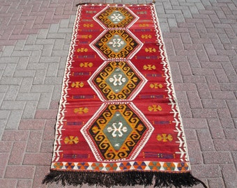May include: A red, white, and black patterned rug with a geometric design. The rug has a fringe border and is made of wool.