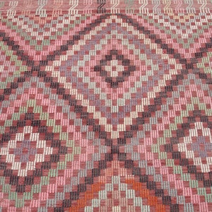 K&ouml;nnte beinhalten: Nahaufnahme eines rosafarbenen, gr&uuml;nen und schwarzen Teppichs mit geometrischem Muster. Der Teppich hat eine gewebte Textur und eine Diamantform in der Mitte.