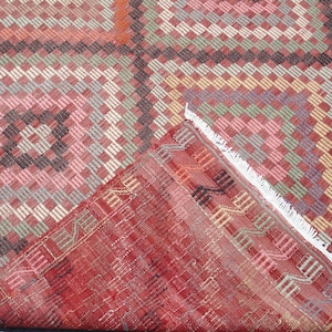 K&ouml;nnte beinhalten: Ein roter, rosa, gr&uuml;ner und schwarzer Teppich mit einem wei&szlig;en Fransenrand. Der Teppich ist in der Mitte gefaltet, so dass die R&uuml;ckseite sichtbar ist.