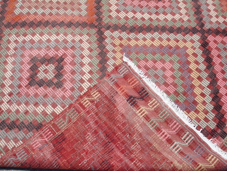 K&ouml;nnte beinhalten: Ein roter, rosa, gr&uuml;ner und schwarzer Teppich mit einem wei&szlig;en Fransenrand. Der Teppich ist in der Mitte gefaltet, so dass die R&uuml;ckseite sichtbar ist.