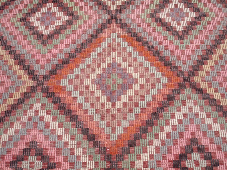 K&ouml;nnte beinhalten: Nahaufnahme eines gewebten Teppichs mit einem geometrischen Muster in den Farben Rosa, Rot, Orange, Gr&uuml;n und Schwarz.