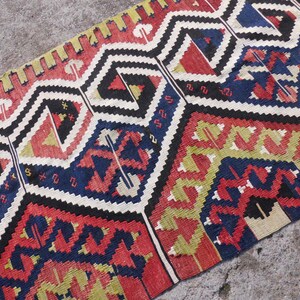 May include: A colorful woven rug with a geometric pattern in shades of red, blue, yellow, and white. The rug has a traditional design with intricate details.