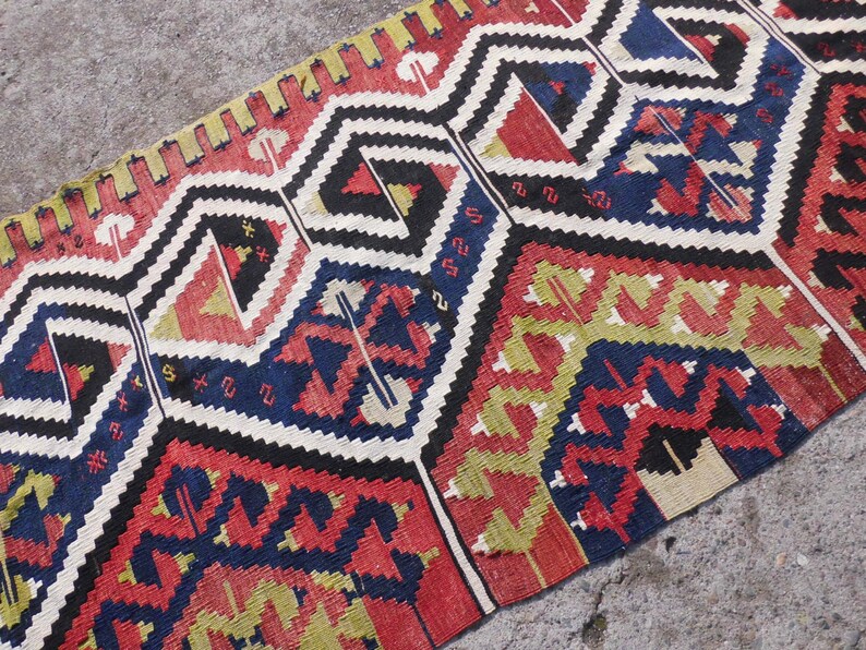 May include: A colorful woven rug with a geometric pattern in shades of red, blue, yellow, and white. The rug has a traditional design with intricate details.