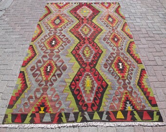 May include: A traditional Turkish rug with a geometric pattern in shades of red, green, yellow, and brown. The rug has a fringe border.