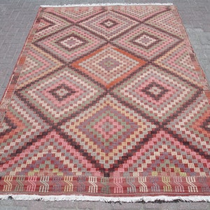 K&ouml;nnte beinhalten: Ein traditioneller t&uuml;rkischer Teppich mit einem geometrischen Muster in Rot-, Braun-, Beige- und Rosat&ouml;nen. Der Teppich hat ein rautenf&ouml;rmiges Design mit filigranen Details.