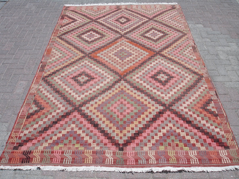K&ouml;nnte beinhalten: Ein traditioneller t&uuml;rkischer Teppich mit einem geometrischen Muster in Rot-, Braun-, Beige- und Rosat&ouml;nen. Der Teppich hat ein rautenf&ouml;rmiges Design mit filigranen Details.
