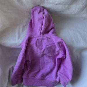 Może przedstawiać: Fioletowa bluza z kapturem dla dziecka. Bluza jest wykonana z miękkiego, wygodnego materiału i ma luźny kr&oacute;j.