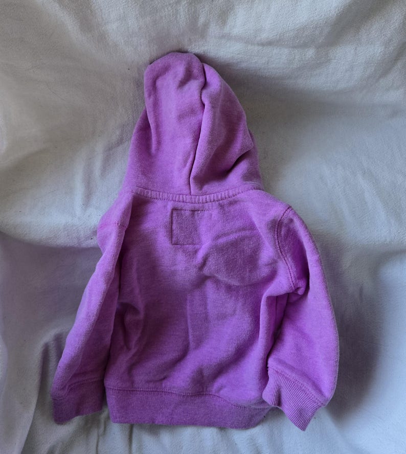 Może przedstawiać: Fioletowa bluza z kapturem dla dziecka. Bluza jest wykonana z miękkiego, wygodnego materiału i ma luźny kr&oacute;j.