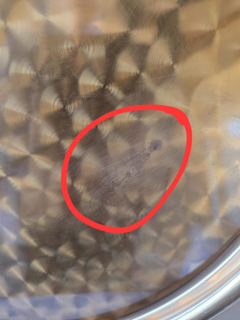 Może przedstawiać: Zbliżenie na stalowy garnek ze śladem po zarysowaniu w kształcie koła na dnie.