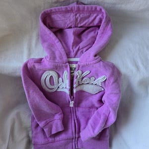 Może przedstawiać: Fioletowa bluza z kapturem zapinana na zamek błyskawiczny z białym logo "Old Navy" z przodu.