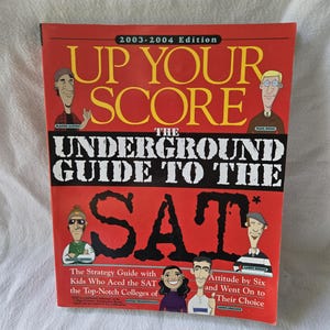 May include: Book cover with a red background and the title "Up Your Score The Underground Guide to the SAT". The cover features cartoon illustrations of people and the text "The Strategy Guide with Kids Who Aced the SAT and Went On to the Top-Notch Colleges of Their Choice."