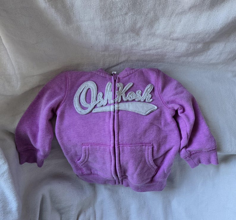 Może przedstawiać: Fioletowa bluza z kapturem i zamkiem błyskawicznym z białym logo OshKosh z przodu.