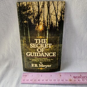 May include: A vintage book titled "THE SECRET OF GUIDANCE" by F.B. Meyer. The cover features a forest scene with a sunset. The book includes practical guidelines for determining where God wants you and what He wants you to do. A ruler is placed at the bottom.