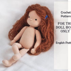 Puede incluir: Una muñeca de ganchillo con piel clara y largo cabello castaño rojizo ondulado con una pequeña pinza azul. El texto a la derecha dice: Crochet Pattern FOR THE DOLL BODY ONLY English Pattern. La muñeca tiene ojos negros y una nariz pequeña.