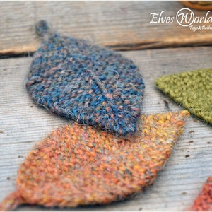 Può includere: Tre forme di foglie a maglia in diversi colori: blu, arancione e verde. Le foglie sono realizzate con una maglia testurizzata e hanno un aspetto peloso.