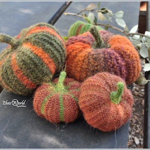 May include: Four knitted pumpkins in various shades of orange, green, and brown. The pumpkins are striped and have a textured surface.